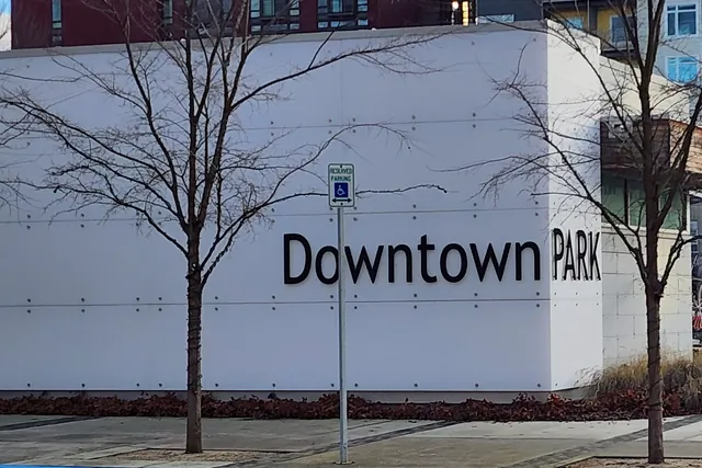 A large white wall with the words Downtown Park in black letters, with young trees and a paved walk in front.